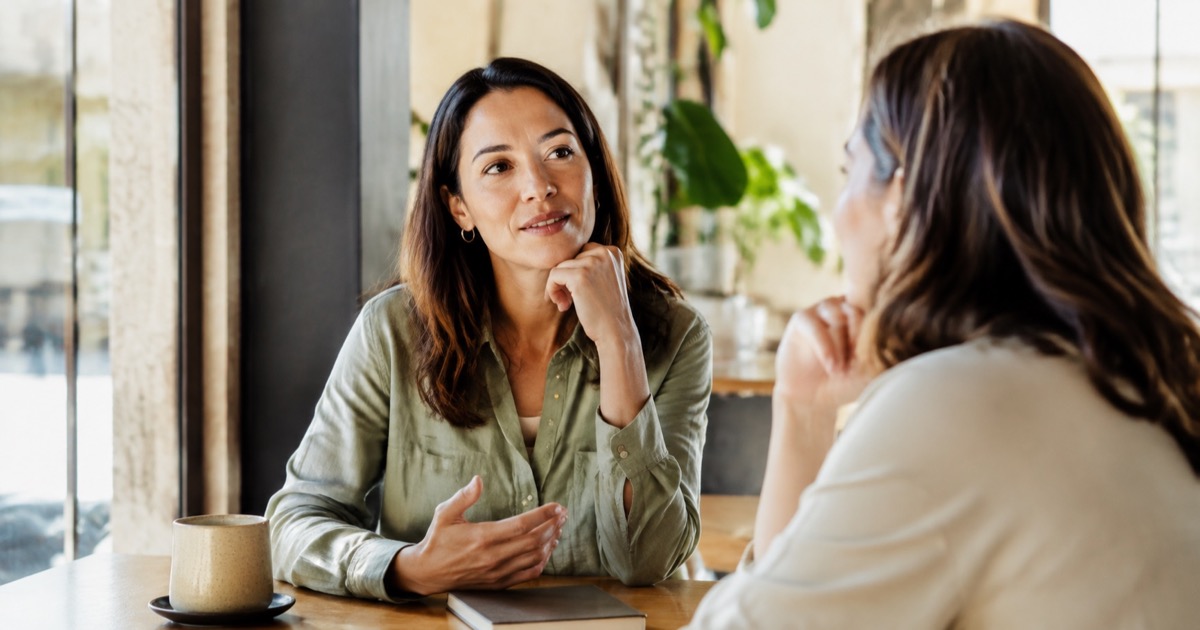A woman practicing a spoken answer with a mentor at a cafe table.