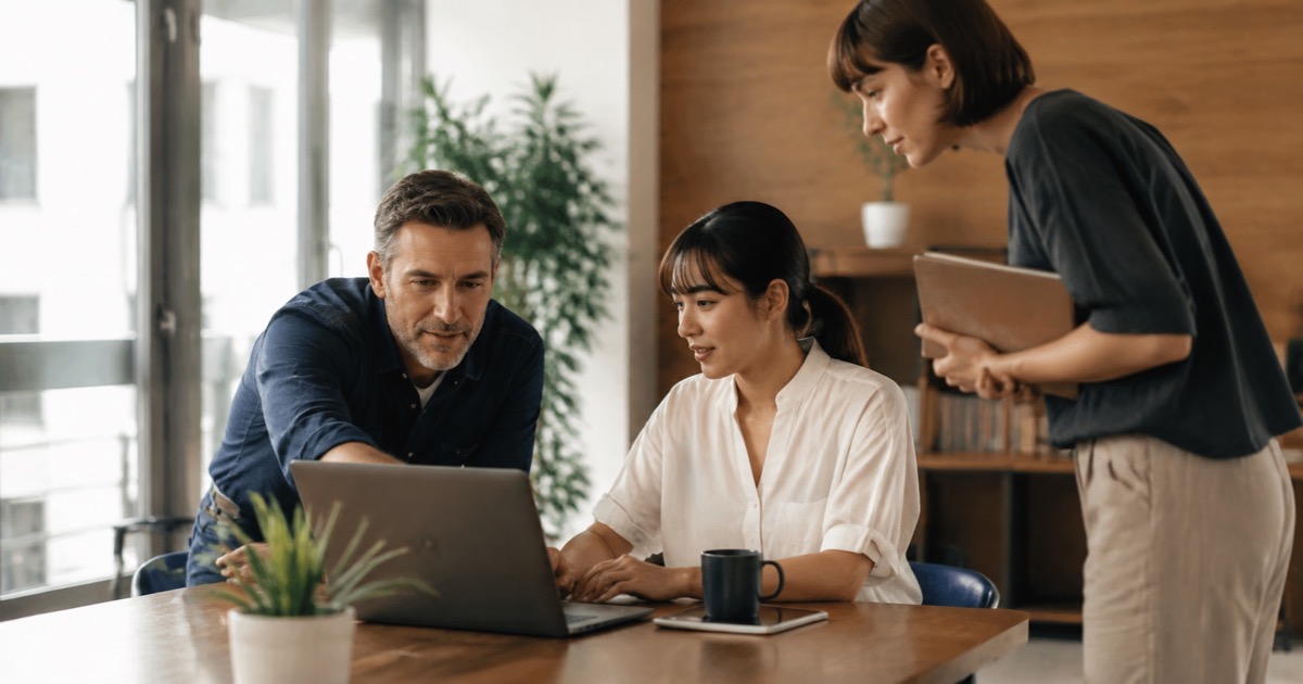 A manager and colleagues reviewing a project at an office workstation.